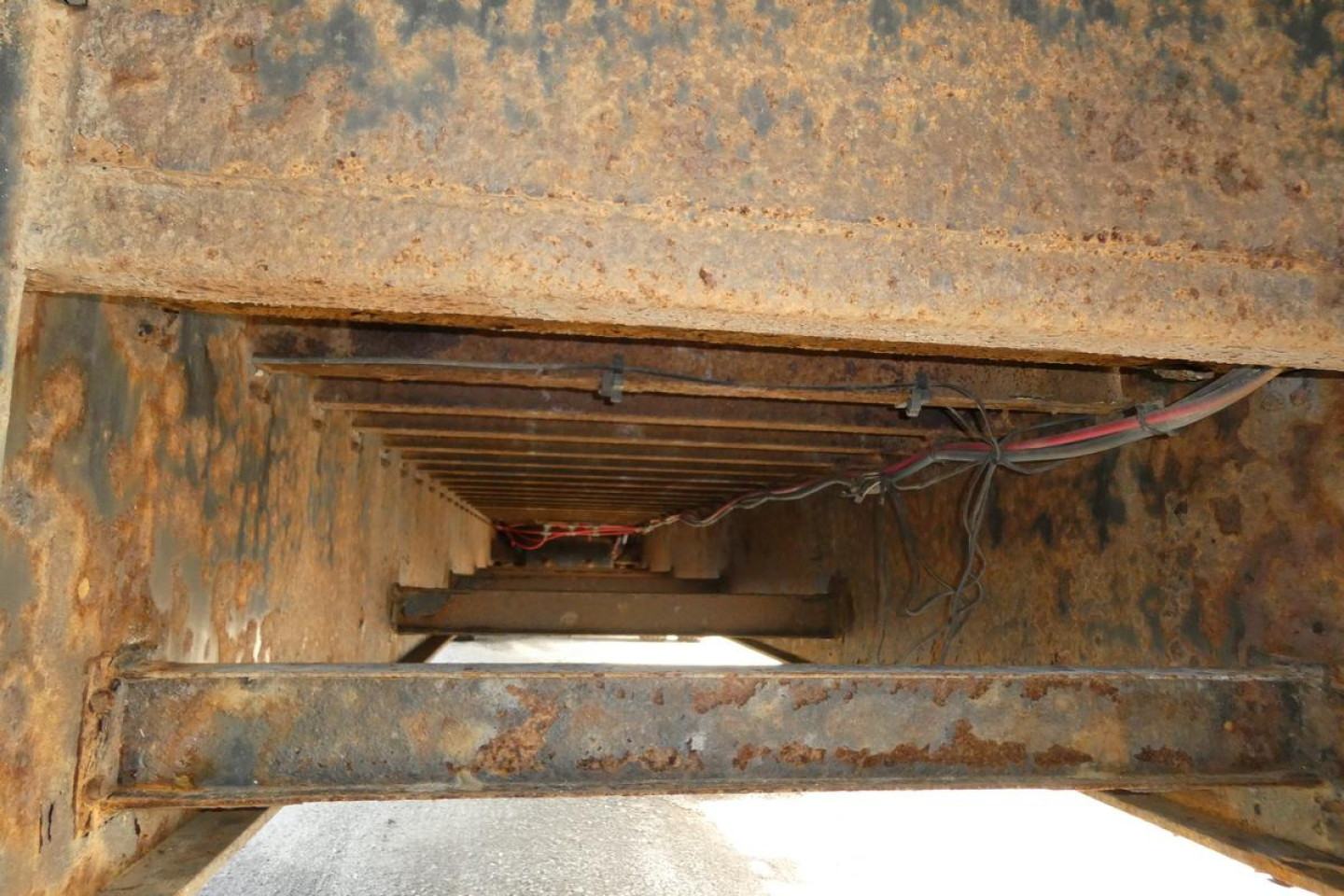 Underbody view of a rusted trailer frame with exposed wiring and beams.