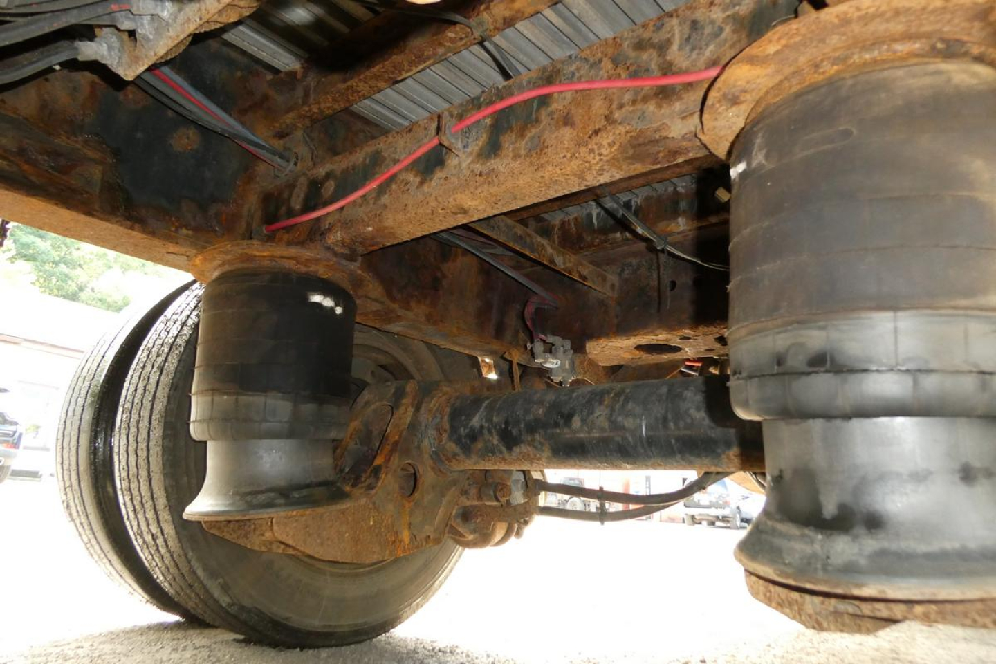 Trailer underside showing air springs and landing gear with rust and wheel near the frame; close-up view of suspension components.