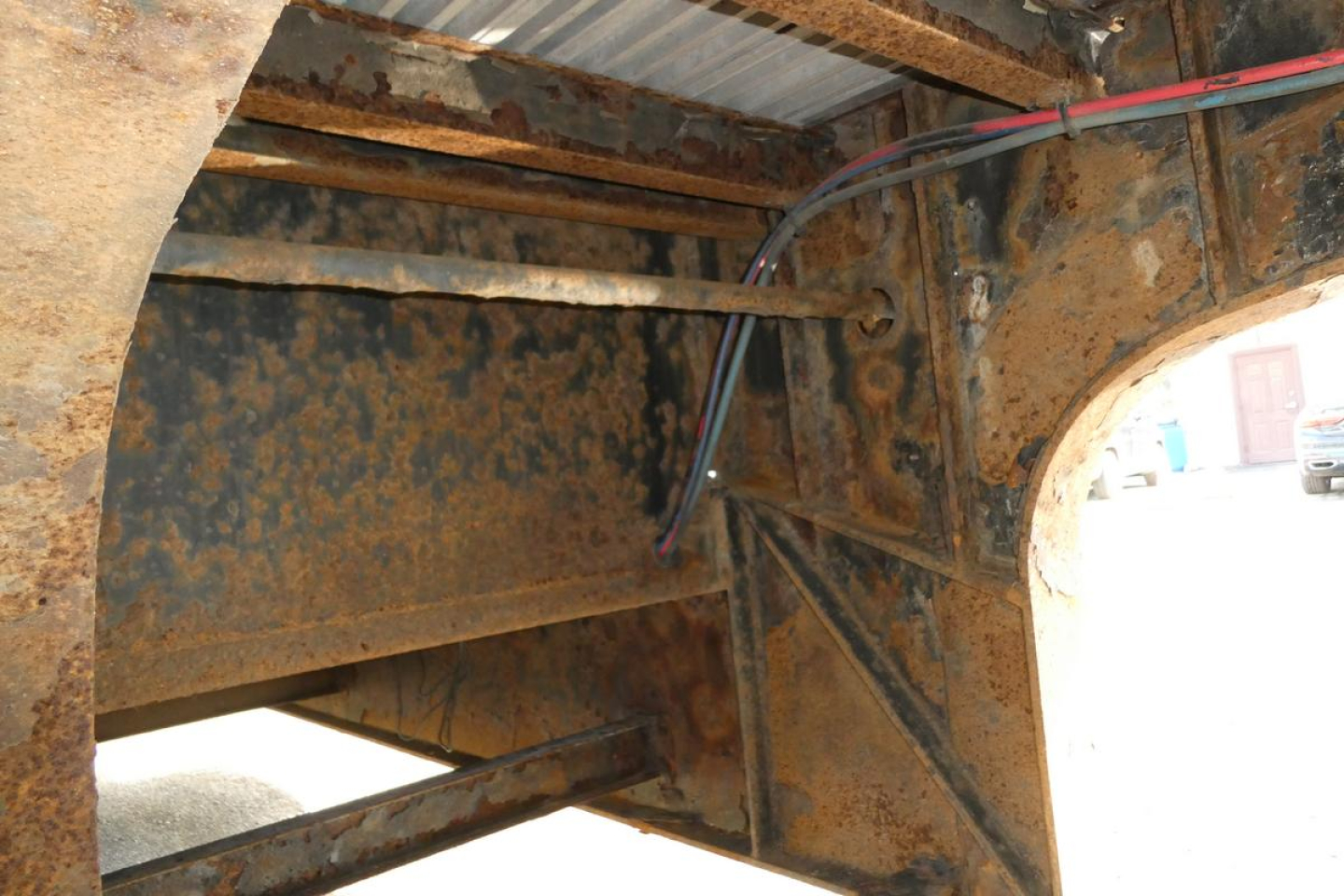Trailer undercarriage showing rusted steel frame and support beams with wiring harness and brackets.
