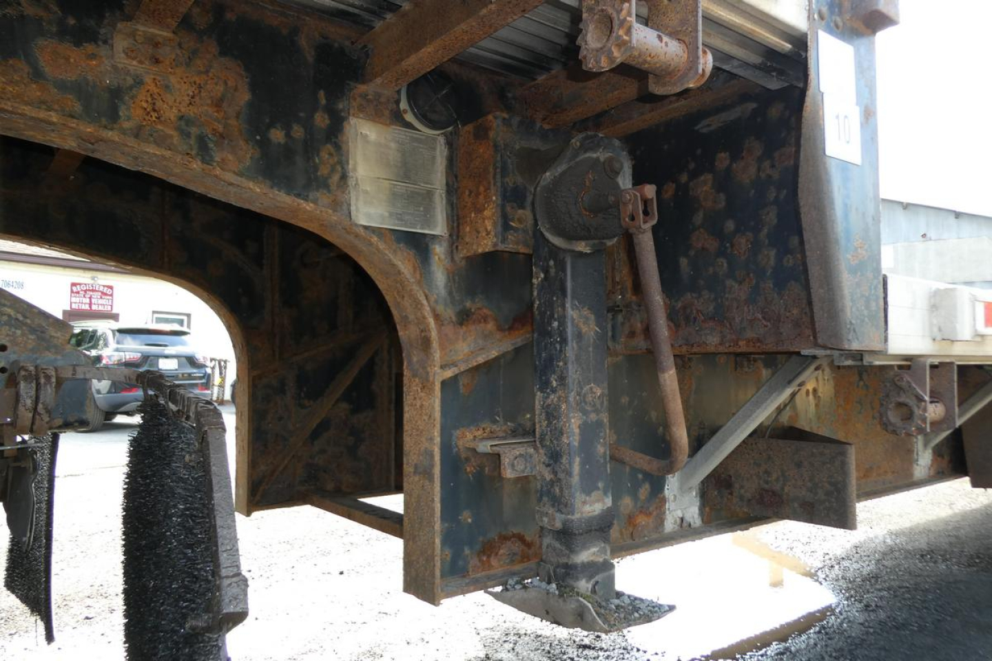 Trailer frame underside showing rusted metal beams and landing gear with support leg and hitch area.