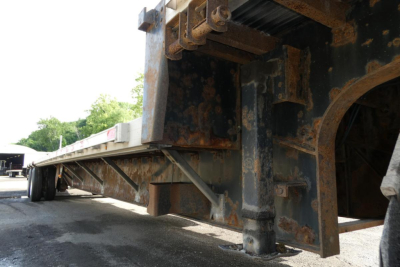 Ground-level view of a steel drop deck trailer chassis showing rusted undercarriage and support beams.