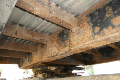 Rusty steel frame and support beams under a drop deck trailer showing rust and structural members.