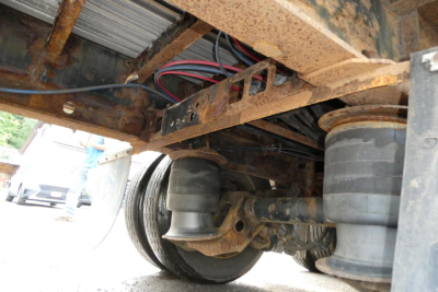 Underneath view of a Great Dane FLD002400053 trailer chassis showing suspension leaf springs and air bags with rusted frame.
