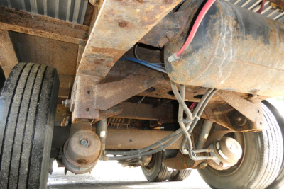 Underbelly of a 2014 Great Dane FLD002400053 trailer showing axles, suspension, and frame with rust-like residue and wiring. Visible components include dual rear axles, leaf springs, wheels, and a large cylindrical tank or pipe running alon