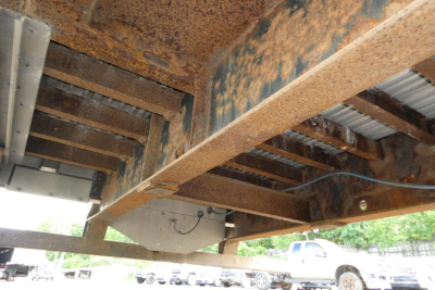 Trailer undercarriage showing rusty steel frame and deck supports with wiring and a gray box.