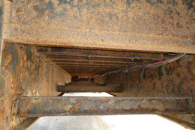 Underbody view of a rusted trailer frame with exposed wiring and beams.