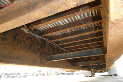 Trailer underside view showing rusted steel frame and support beams of a Great Dane drop deck trailer with wiring harness.