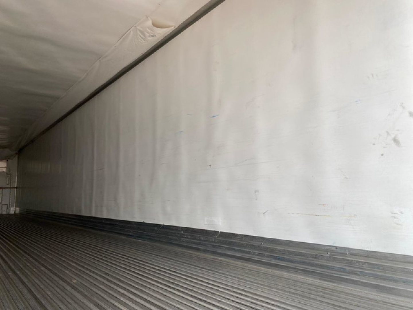 Trailer interior showing white insulated wall and ribbed floor of a refrigerated trailer.