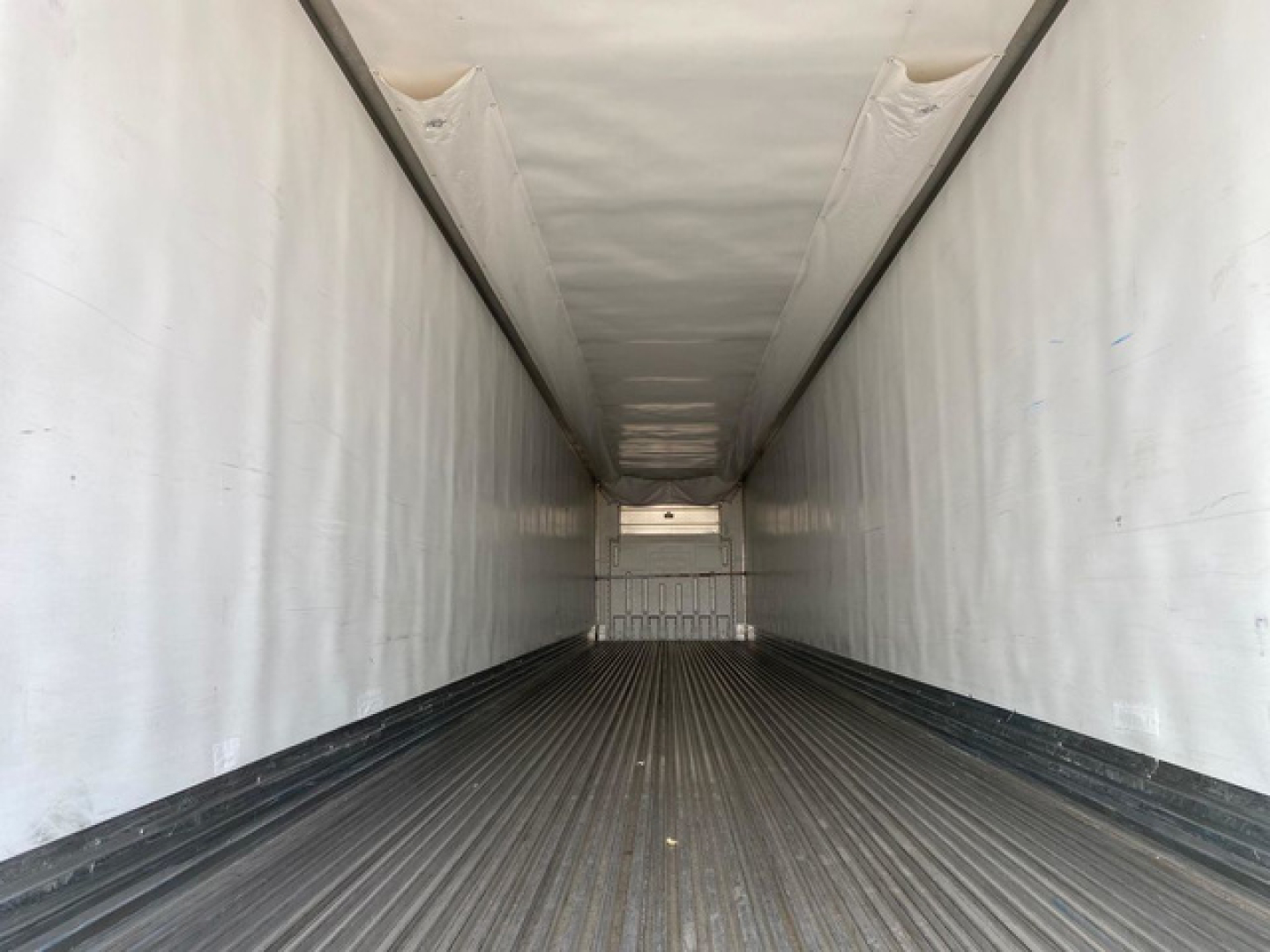 Trailer interior showing long refrigerated cargo area with white insulated walls and a ribbed black floor, empty and viewed from rear doors toward front.