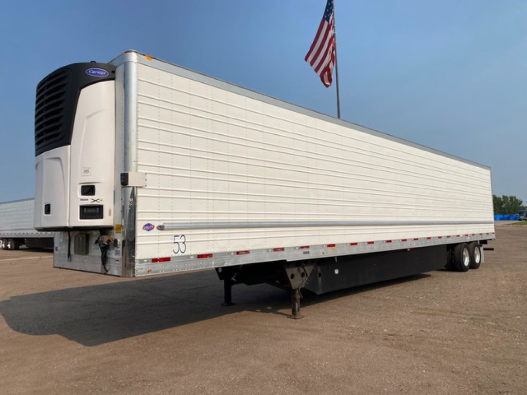 Utility refrigerated trailer with white sides and a blue-framed refrigeration unit at the front, American flag in background, 3-axle setup.