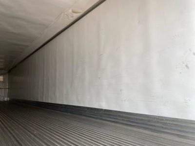 Trailer interior showing white insulated wall and ribbed floor of a refrigerated trailer.
