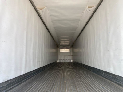 Trailer interior showing long refrigerated cargo area with white insulated walls and a ribbed black floor, empty and viewed from rear doors toward front.
