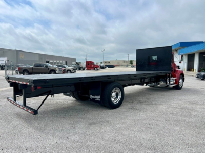 Kenworth flatbed truck in service showing long flatbed with rear tail consider and red cab in background