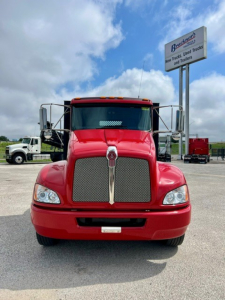 Kenworth T270 front view showing large chrome grille, red cab, and headlights.enkil signage in background reads a dealership. 