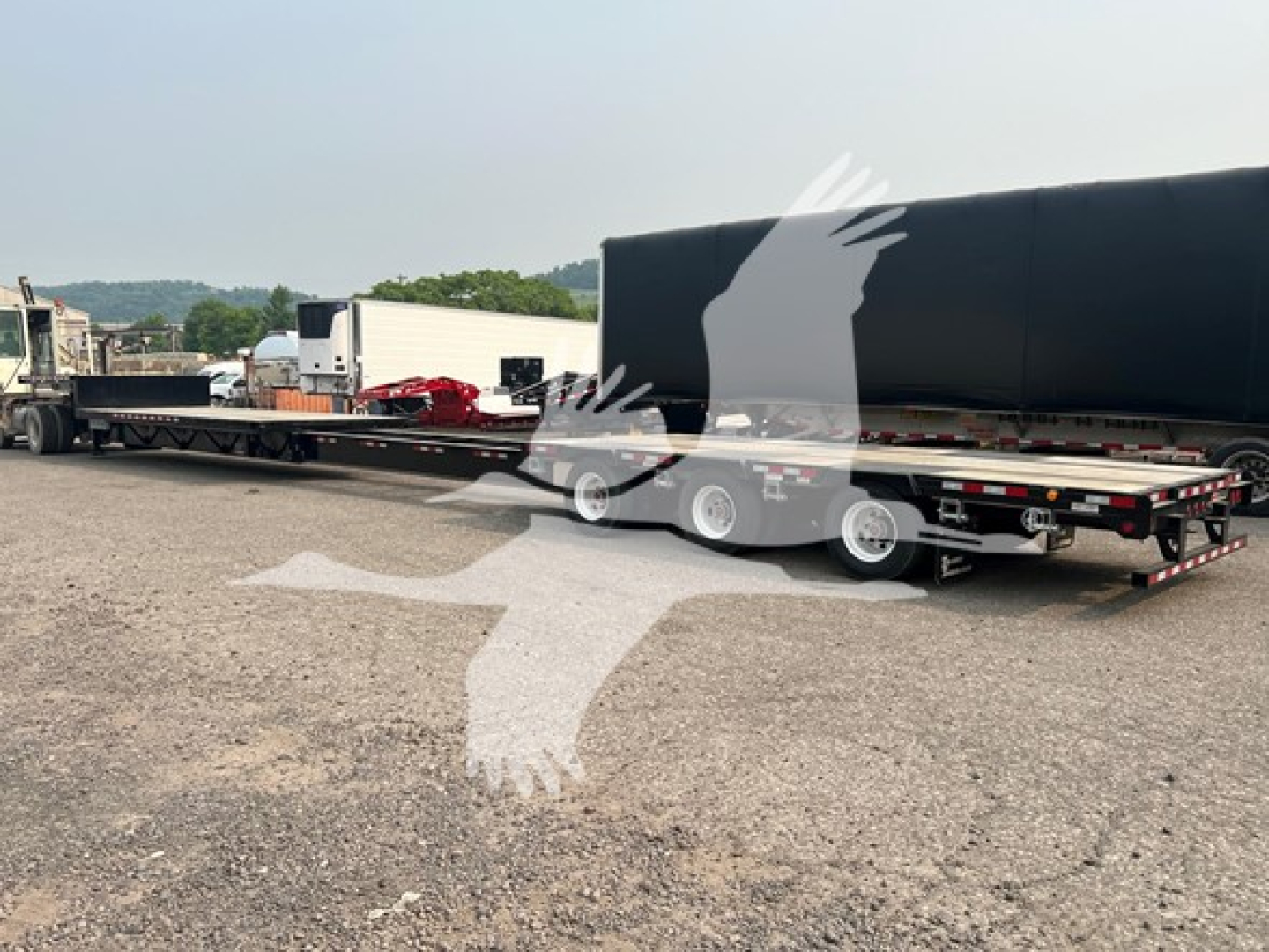 Manac steel drop extendable trailer shown in side view with black gooseneck and multiple axles, chain hookups, and flatbed sections.