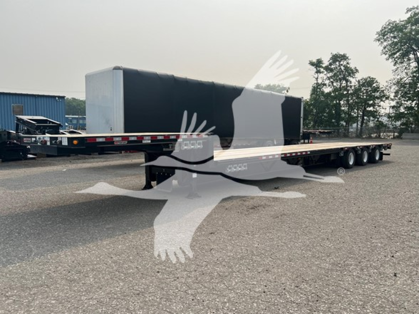 Manac steel drop extendable trailer with black gooseneck and long flat deck showing side decals and tandem axles.