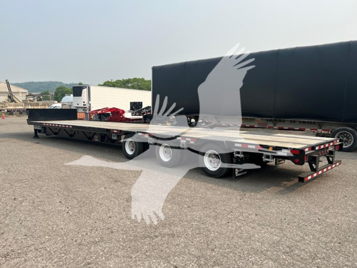 Manac steel drop extendable trailer in a parking lot, side view showing deck and extendable sections with wheels and reflective tape.