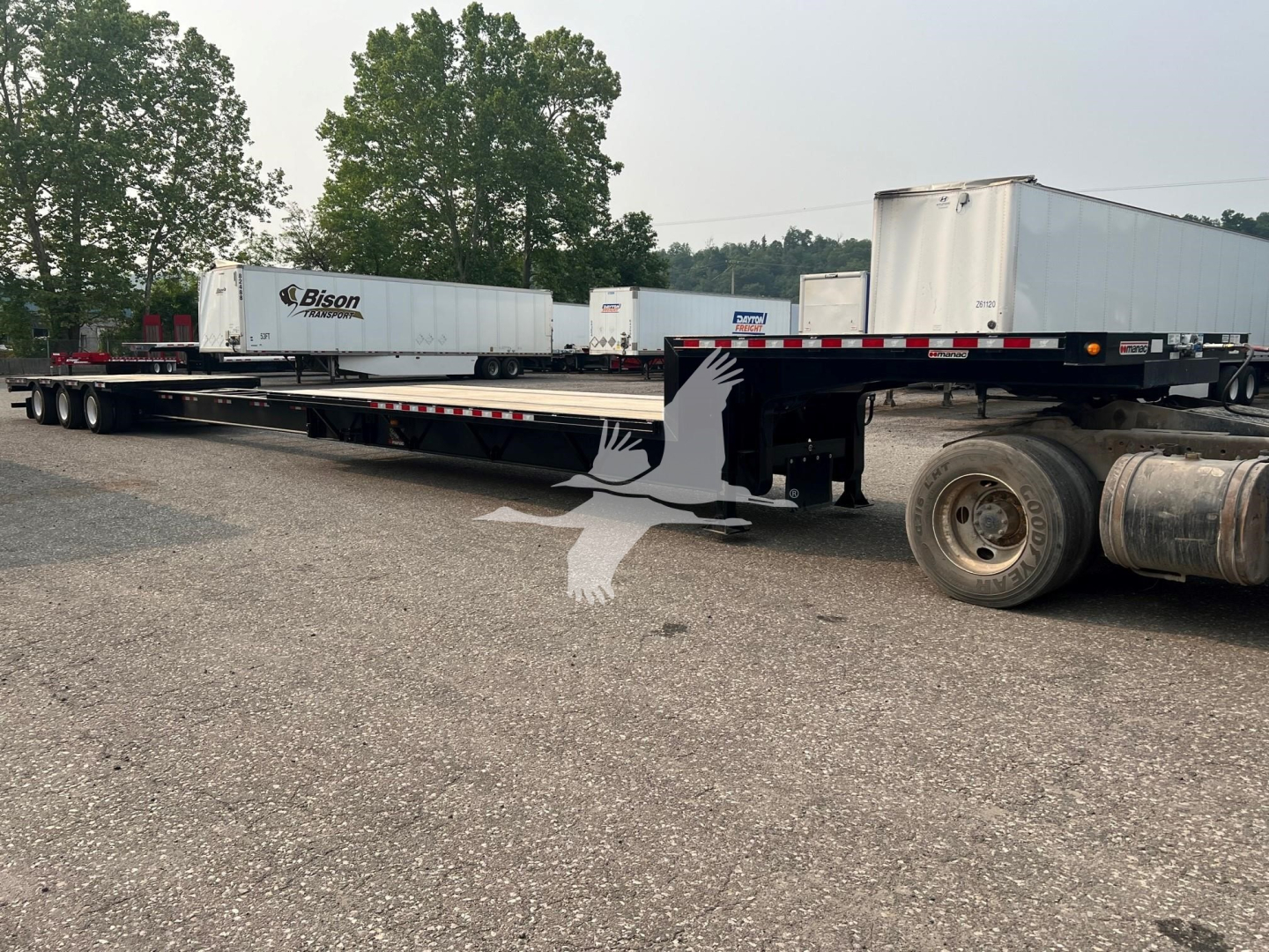 Manac steel drop extendable trailer with multiple trailers in the background; visible text includes Bison trailer logo on a white box and other trailers.