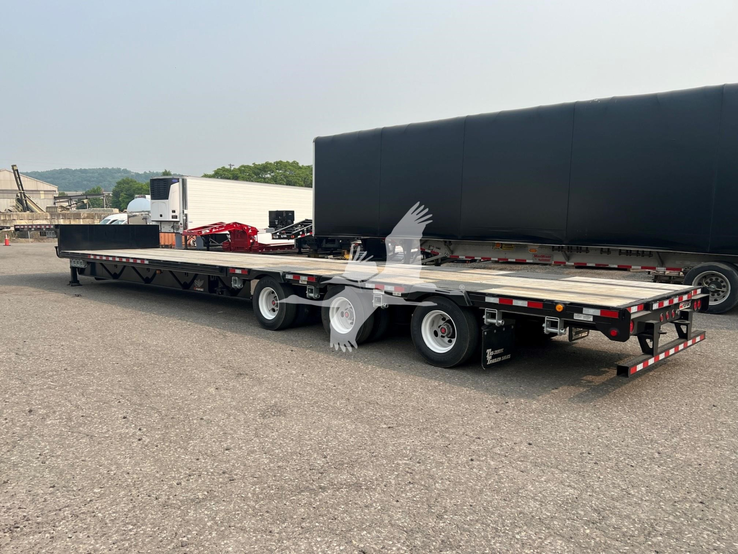 Manac steel drop extendable trailer in a parking lot, side view showing flatbed with dual rear axles and red-and-white reflective stripes.