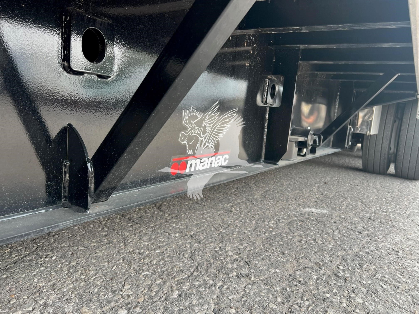 Manac trailer undercarriage showing black steel frame with Manac logo and white eagle graphic; close-up of deck edge and support brackets.