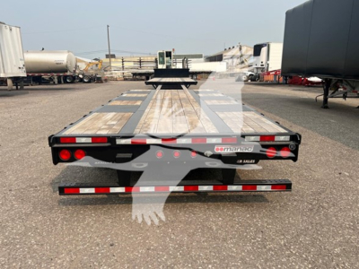 Trailer rear view showing flatbed drop deck 2023 Manac extendable with wood deck, red/white reflective strips and taillights.
