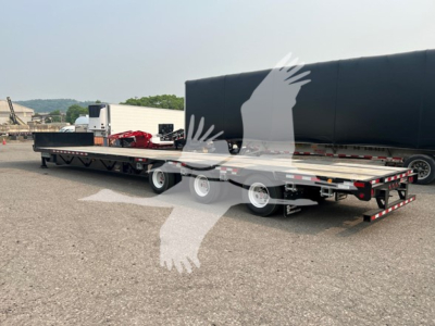 Manac steel drop extendable trailer in a parking lot, side view showing deck and extendable sections with wheels and reflective tape.