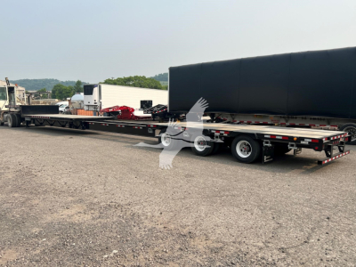 Long steel drop extendable trailer in a yard with a large black tarp cover and other equipment in background.