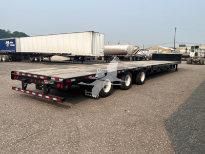 Manac steel drop extendable trailer viewed from rear-left, long flatbed with triple axles and extendable deck, warning lights, and rear bumper.