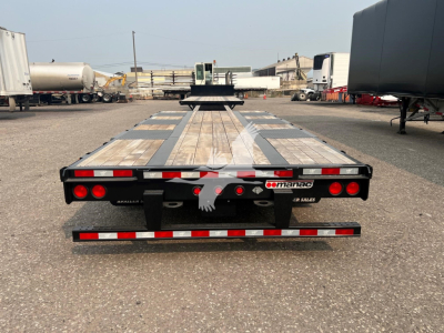 Manac steel drop extendable trailer seen from rear, with wooden deck, reflectors, taillights, and branding plate.