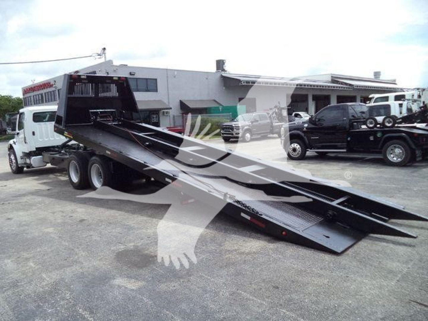 Truck bed with a lowboy tilt trailer in a lot, Freightliner M2 106 environment with multiple vehicles
