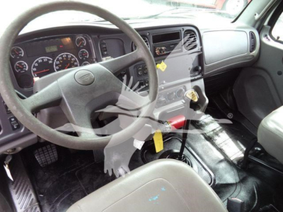 Cab interior of a Freightliner M2 106 showing steering wheel, dashboard with gauges, center console, gear selector, and driver's seat