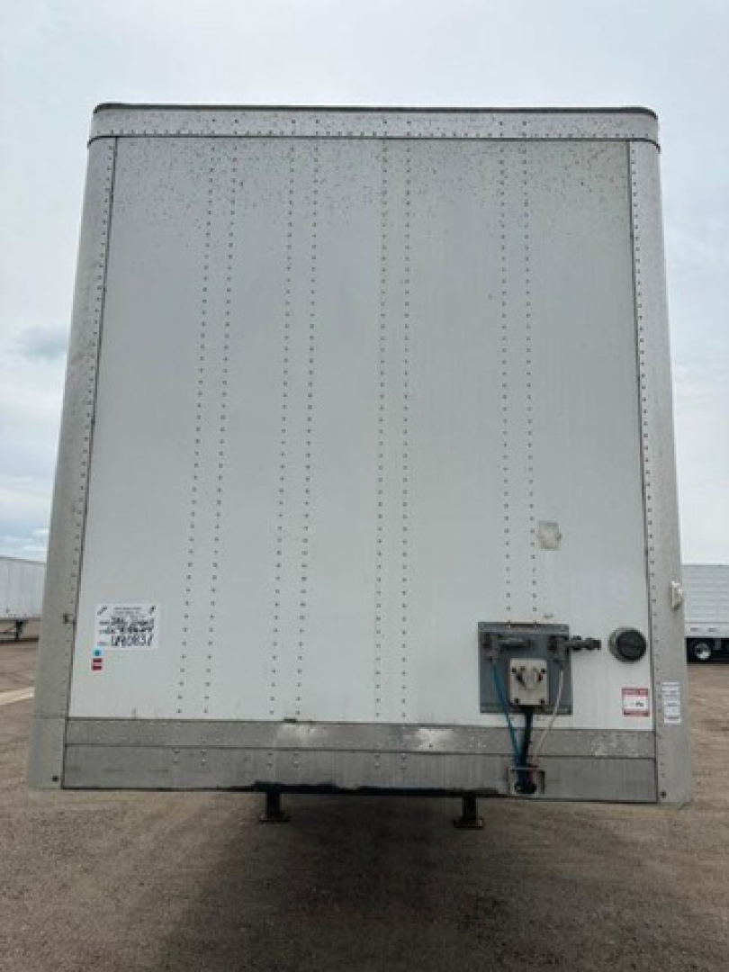 Back view of a 2016 Wabash van trailer with a vertical riveted aluminum panel, rear door hardware, and a hitch area; some small labels near bottom corners.