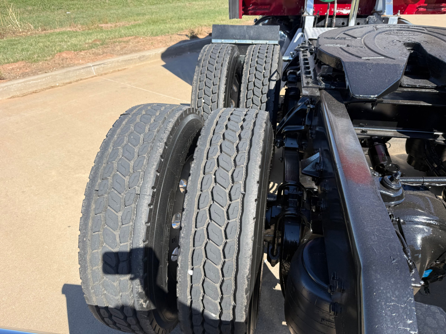Dual rear drive tires on Kenworth truck chassis with visible suspension and fifth wheel, side view.