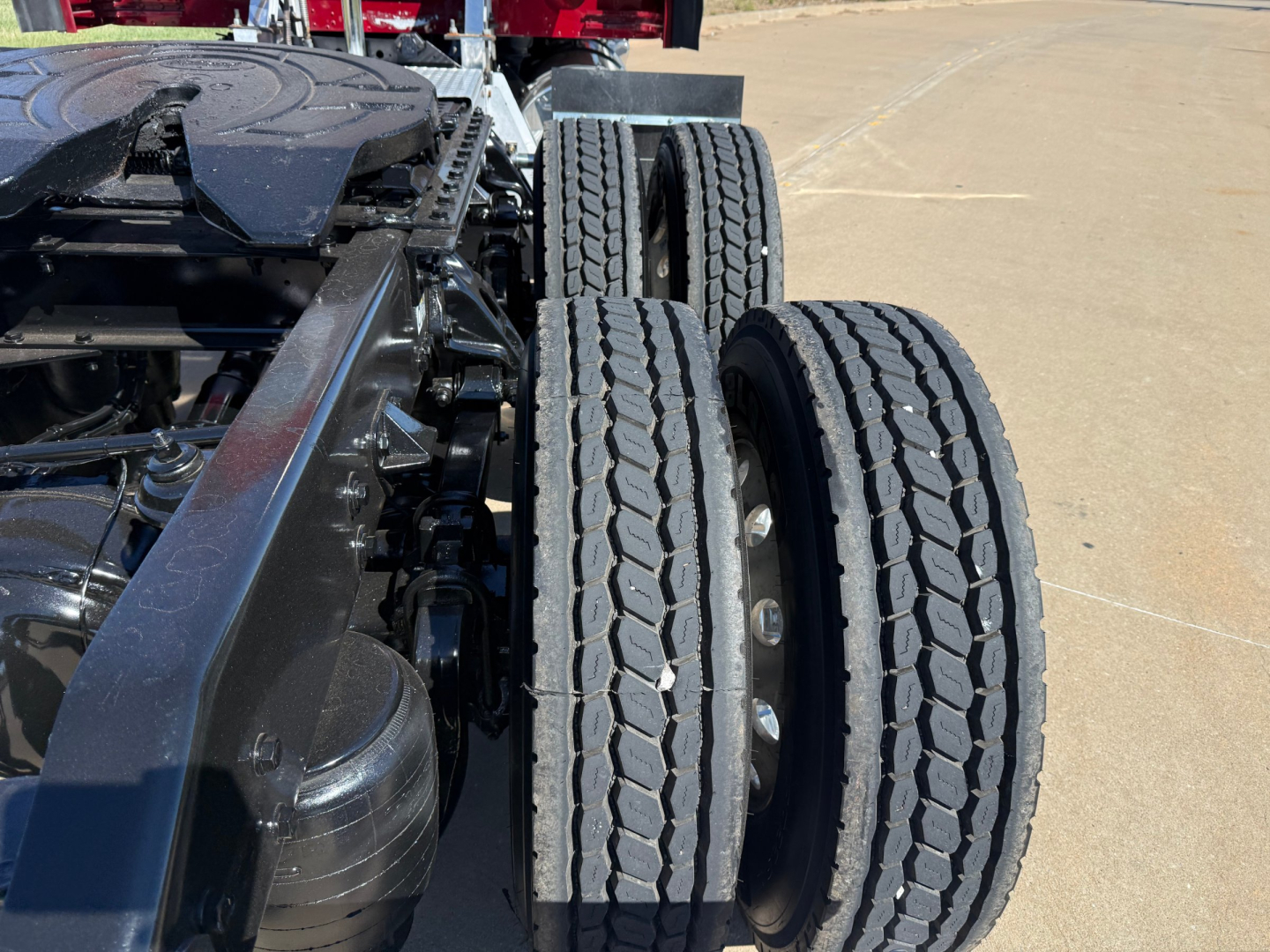Kenworth W900L truck rear wheel assembly showing dual rear axles and tire tread with surrounding chassis components.