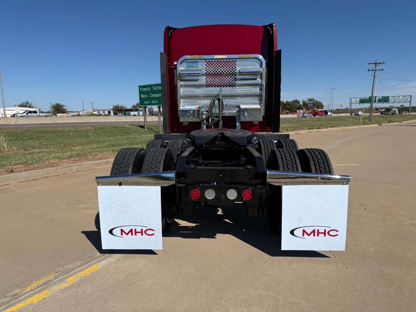 Kenworth W900L rear view showing chassis, dual rear axles, chrome fuel tanks, and mud flaps with MHC logos.