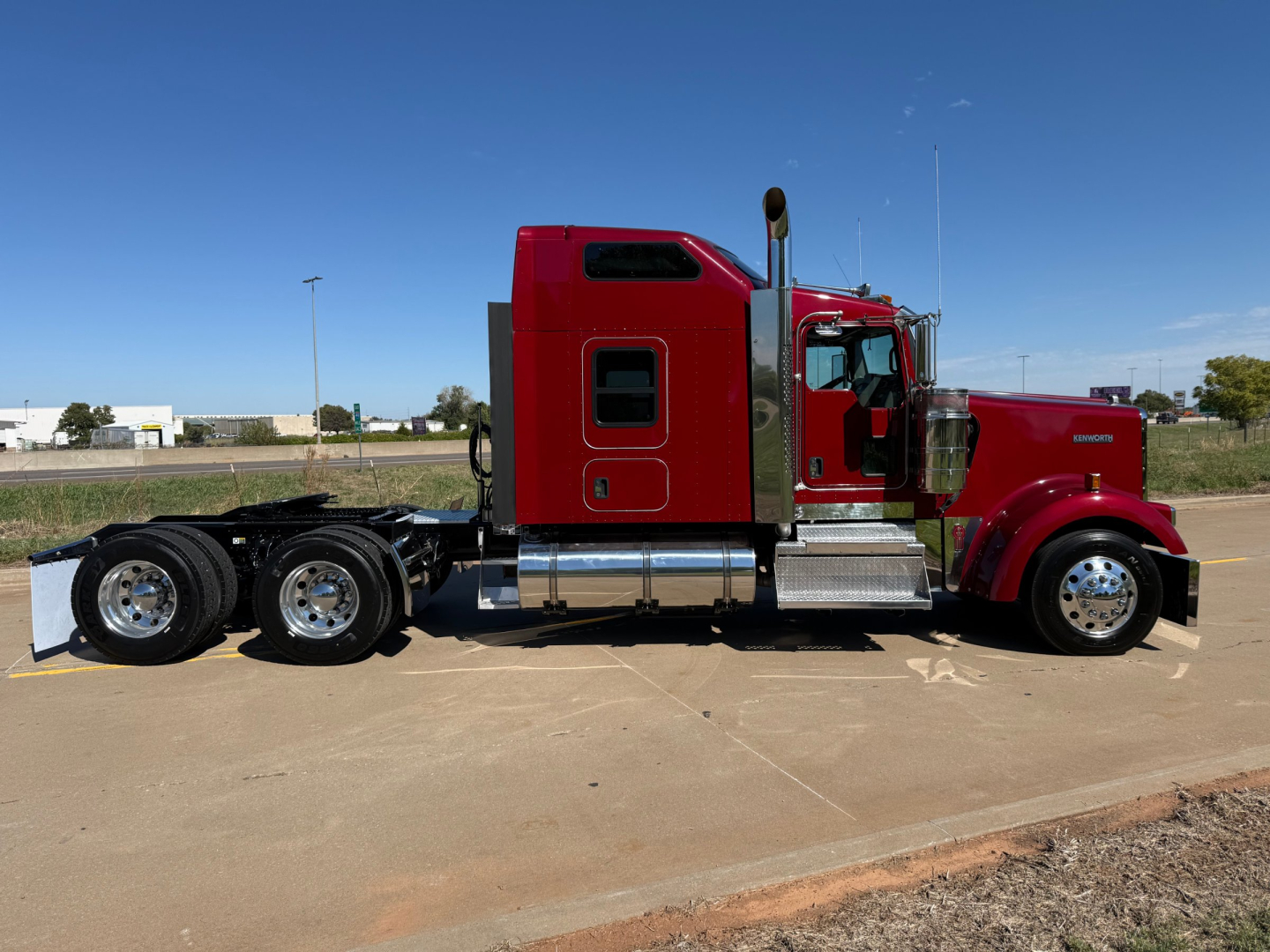 Kenworth W900L sleeper cab truck side profile showing glossy red paint, chrome fuel tanks, and dual rear axles with aluminum steps.