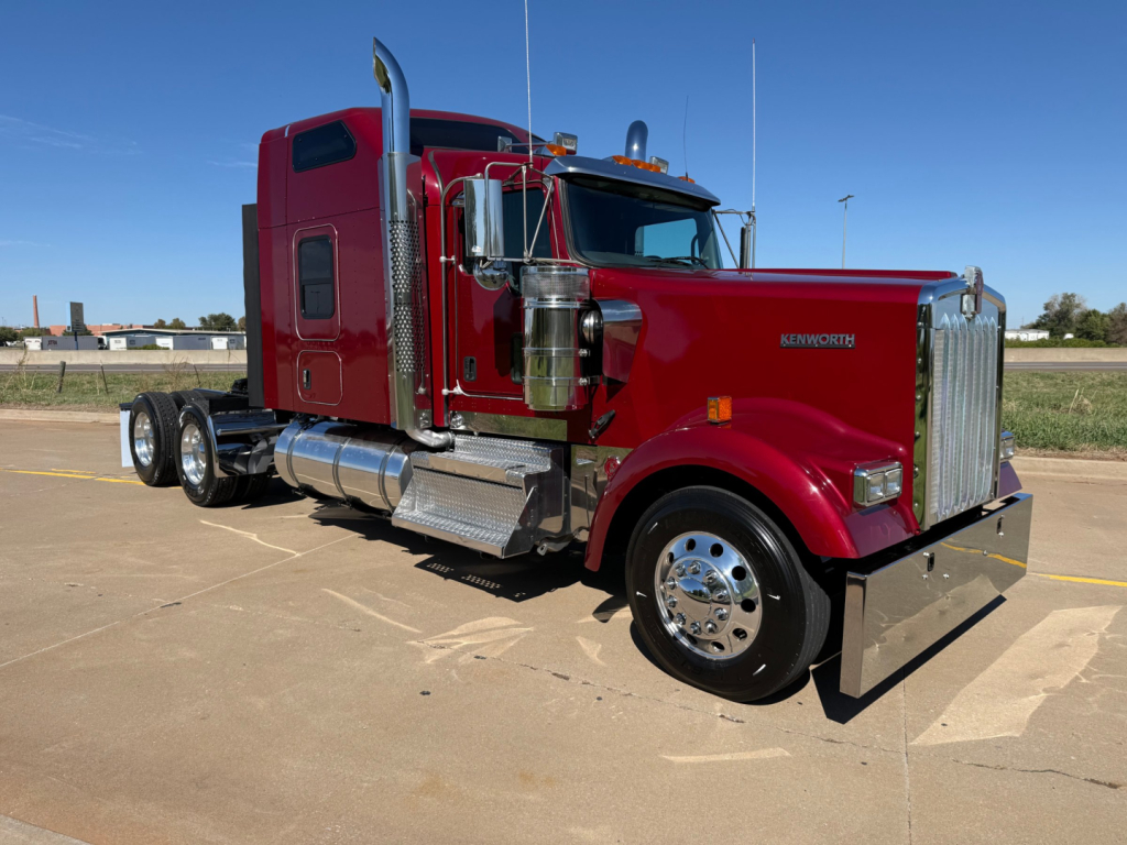 Kenworth W900L truck with maroon cab, chrome exhaust stacks, and polished aluminum fuel tanks. Side view showing front grille, dual rear axles, and chrome wheels.