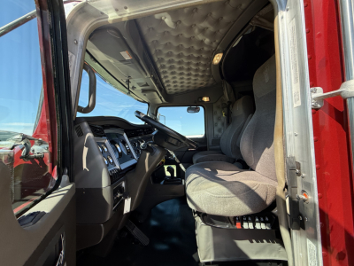 Truck cab interior view from open driver door showing steering wheel, dash, and seating in Kenworth W900L with quilted overhead upholstery.