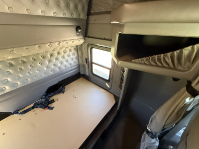 Kenworth W900L sleeper cab interior showing bed platform, quilted wall padding, overhead storage shelf, and window with sunshade band.
