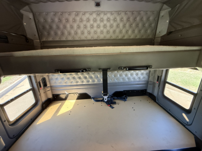 Kenworth W900L sleeper cab interior cargo area with diamond-stitched side panels and overhead storage; rear bed area showing straps and tie-downs.