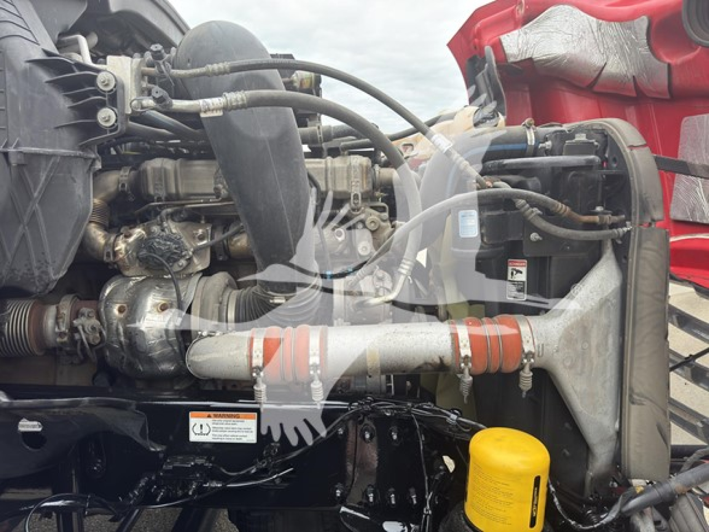 Truck engine bay with radiator, turbocharger, hoses, and intercooler; yellow coolant reservoir cap visible; intake piping and metal brackets; partial pink exterior
