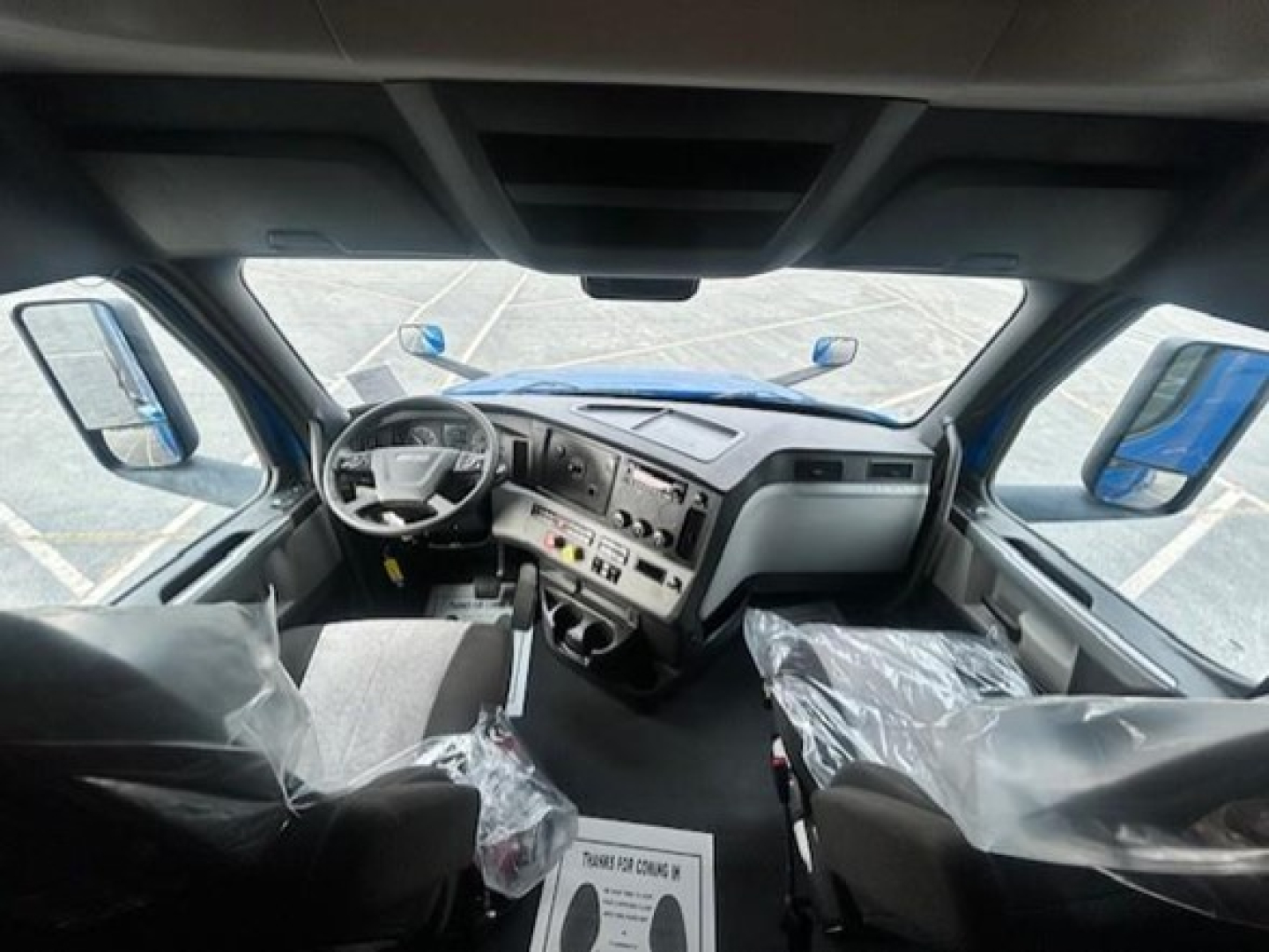 Truck cab interior showing steering wheel and dash with center controls and two front seats wrapped in plastic.