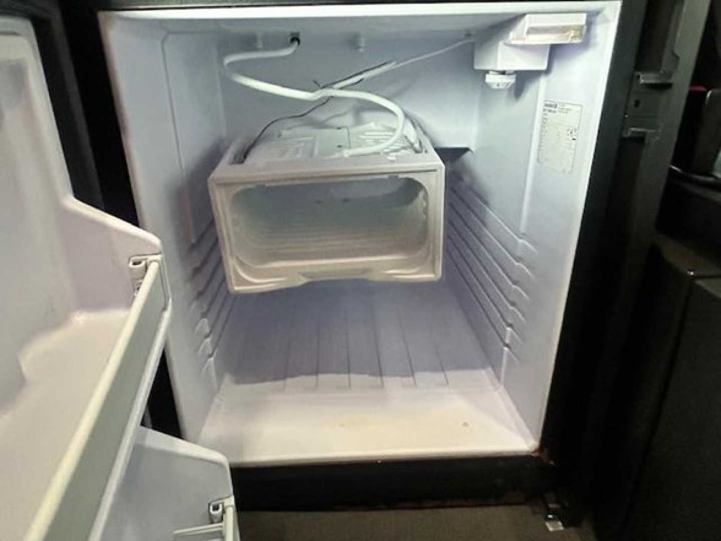 Refrigerator/freezer mounted in Freightliner Cascadia engine bay showing compact unit with freezer compartment and power cord.