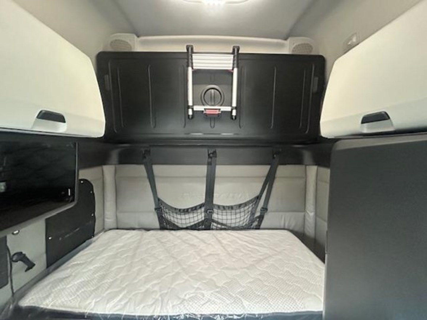 Interior sleeper area of a 2022 Freightliner Cascadia 126 cab showing a diamond quilted mattress, storage net, overhead compartment, and side cabinets.