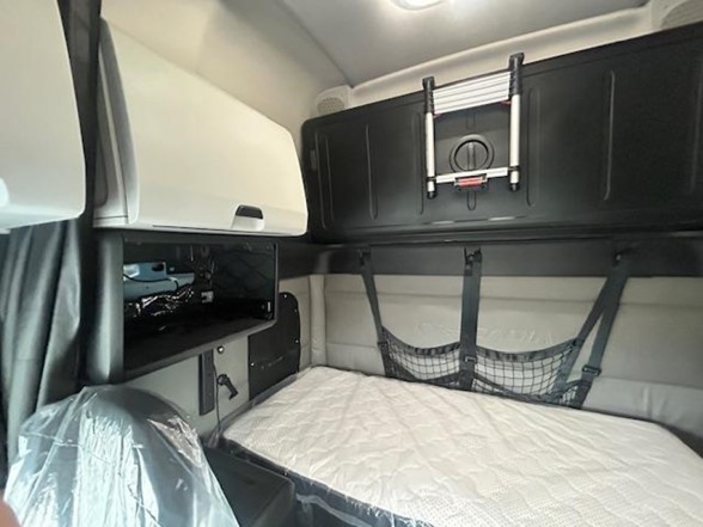 Freightliner Cascadia sleeper cab interior with bed and overhead storage showing network pouch, cabinets, and seat belt strap.