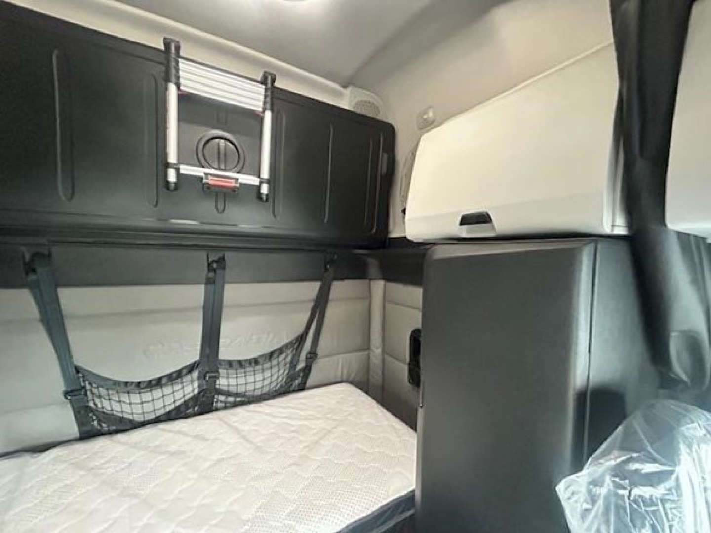 Interior of a 2022 Freightliner Cascadia 126 sleeper cab showing upper storage cabinet, window shade, and sleeper netting over a mattress.