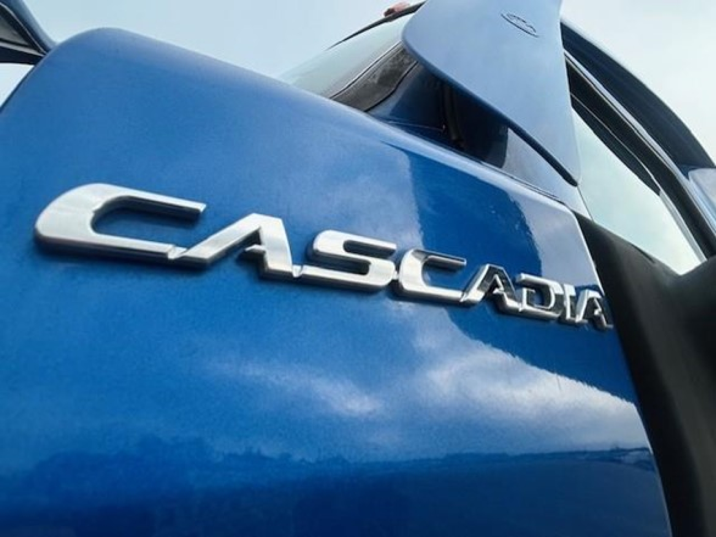 Freightliner Cascadia badge on blue truck door viewed from side, showing 'CASCADIA' lettering.