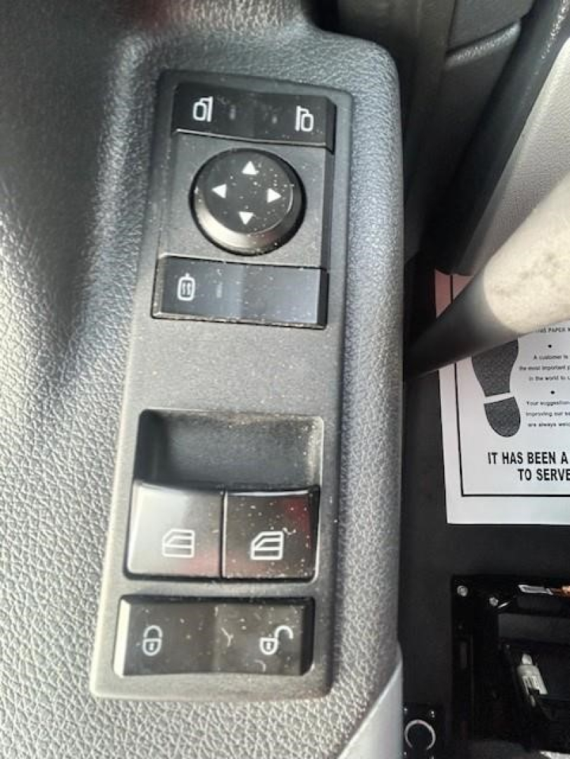Truck interior switch panel with window controls and mirror adjustment on Freightliner Cascadia dash. Visible: circular joystick, two top small buttons, two middle window switch blocks, bottom lock switches.