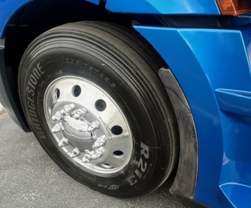 Bridgestone tire on a blue Freightliner Cascadia wheel well showing chrome hub and lug nuts.