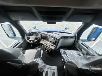 Truck cab interior showing steering wheel and dash with center controls and two front seats wrapped in plastic.